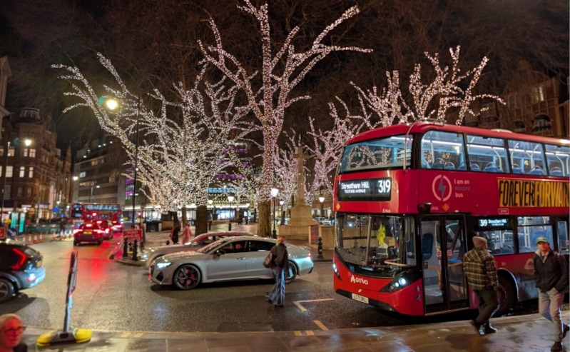 Red London bus against lights in trees